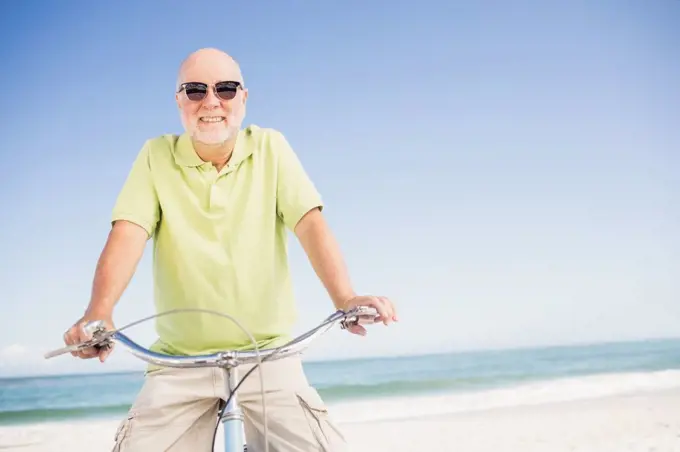 Smiling senior man with bike on the beach