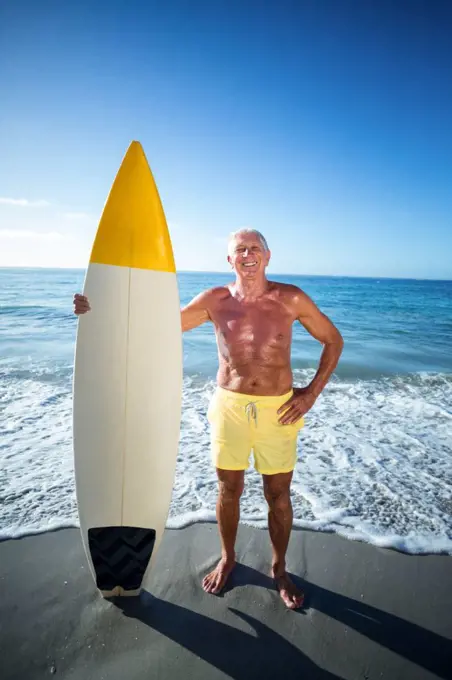 Senior man posing with a surfboard at the beach