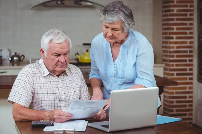 Retired couple calculating bills with laptop at home