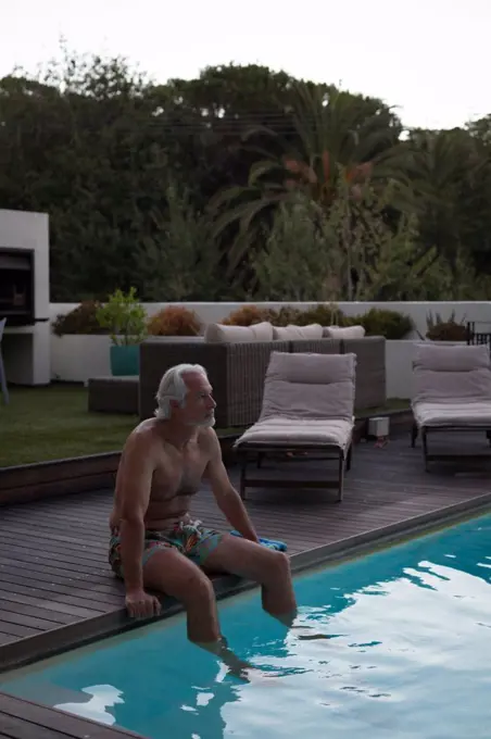 Active senior man sitting at the edge of swimming pool
