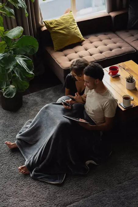 Couple using mobile phone and digital tablet in living room at home
