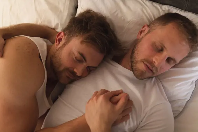 High angle view close up of Caucasian male couple relaxing at home, lying in a bed, embracing and sleeping together.