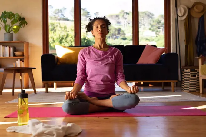Caucasian woman with eyes closed meditating, practicing yoga at home. Staying at home in self isolation during quarantine lockdown.