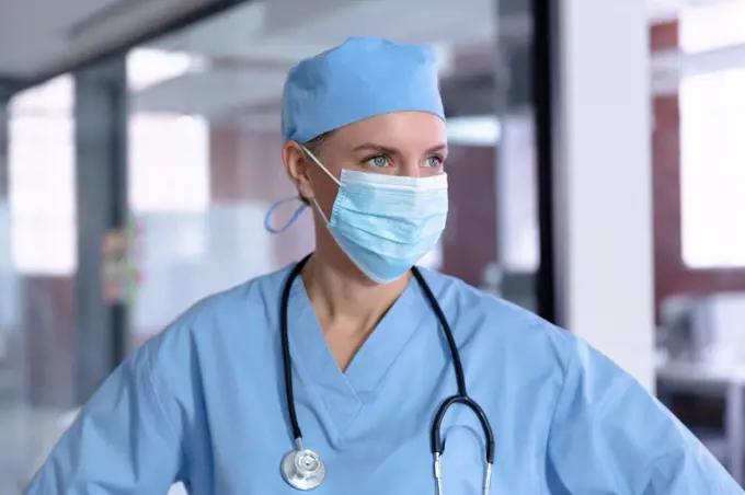 Caucasian female doctor wearing face mask, scrubs and stethoscope looking away. medical professional at work during coronavirus covid 19 pandemic.