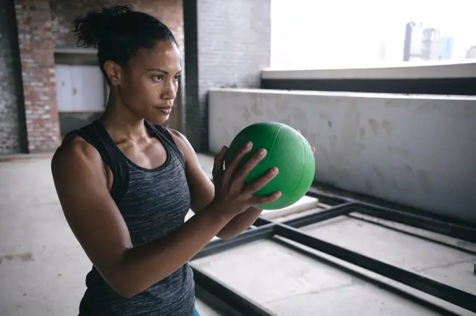 Determined fit african american woman exercising holding volleyball ball in empty warehouse space. urban fitness and sport.