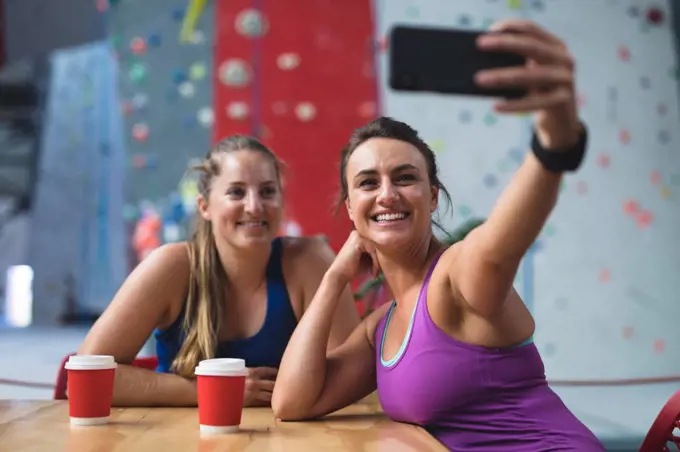 Two happy caucasian women taking selfie with smartphone in cafe at indoor climbing wall. fitness and leisure time at gym.