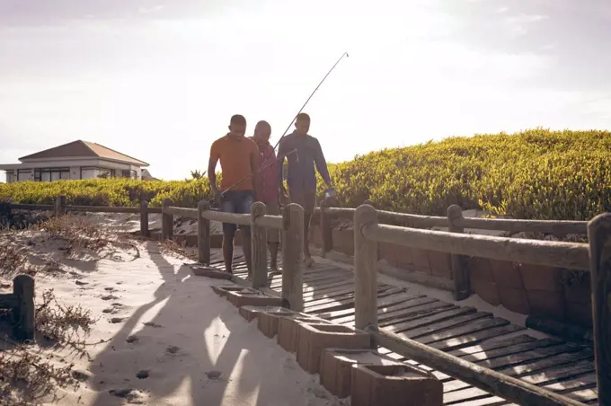 African american father and his two sons with fishing rods walking together on the bridge. summer beach holiday and leisure concept.