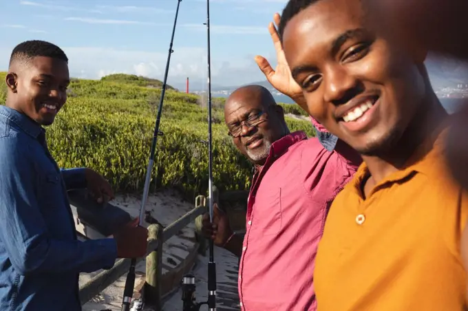 African american father and his two sons smiling together while taking a selfie on the bridge. summer beach holiday and leisure concept.