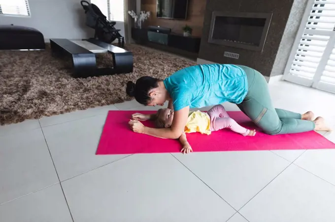 Caucasian mother performing plank exercise while baby under her at home. motherhood, love and baby care concept