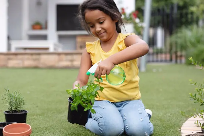 Smiling hispanic girl gardening, kneeling and watering plant in pot. family spending time together at home.