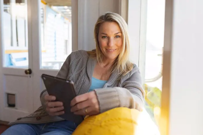 Happy caucasian mature woman using tablet in sunny living room. enjoying leisure time at home.