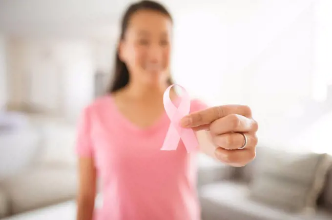 Asian woman in pink tshirt showing breast cancer awareness pink ribbon at home. health, prevention and breast cancer awareness.