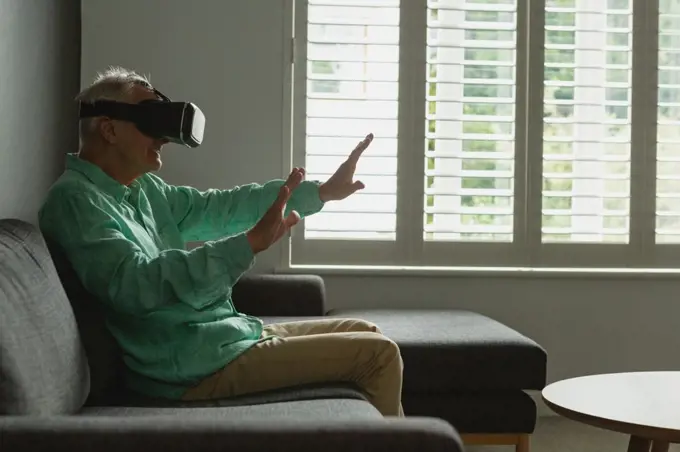 Side view of active senior Caucasian man using virtual reality headset in living room at home