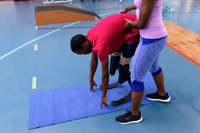Side view of African-american female trainer assisting disabled African-american man while exercising in sports center. Sports Rehab Centre with physiotherapists and patients working together towards healing