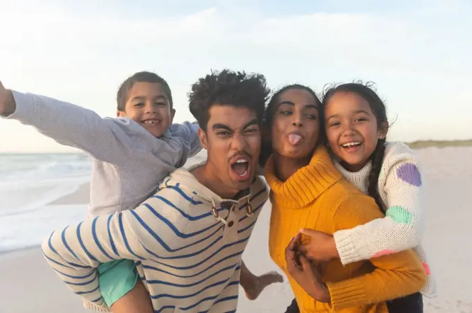 Mischievous multiracial parents giving piggyback rides to children at beach during sunset. family, lifestyle and weekend.