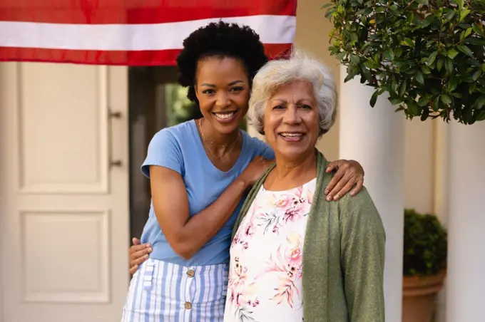 Portrait of smiling african american daughter with arm around mother at house entrance. family and bonding, unaltered
