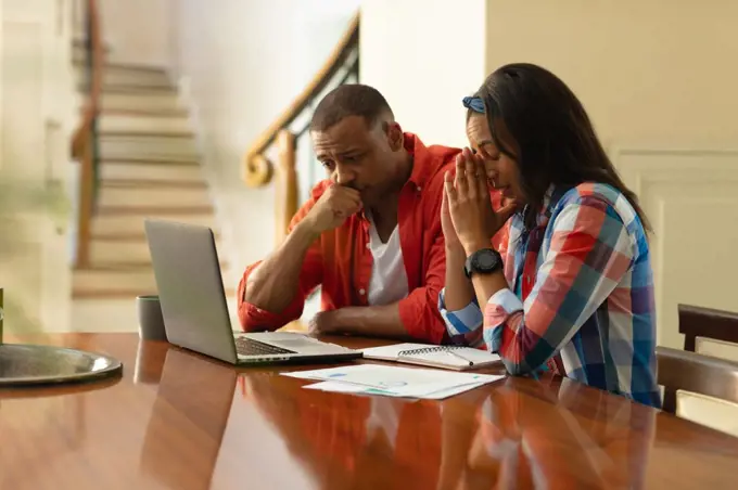 African american couple looking at laptop while sitting with financial bills at home. people, togetherness and home finance concept, unaltered.