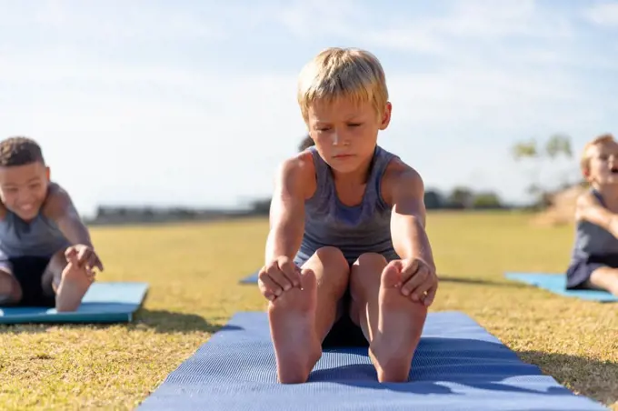 Multiracial elementary schoolboys touching toes while exercising on yoga mat in school ground. unaltered, childhood, education, activity, sports training, yoga and physical education concept.