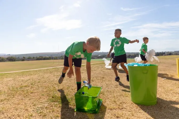 Multiracial elementary schoolboys putting plastic garbage in garbage bin on school ground. unaltered, sustainable lifestyle, teamwork, cleaning, responsibility and recycling concept.