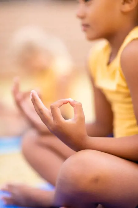Biracial elementary schoolgirl meditating while sitting on ground. unaltered, childhood, education, activity, sports training, yoga and physical education concept.
