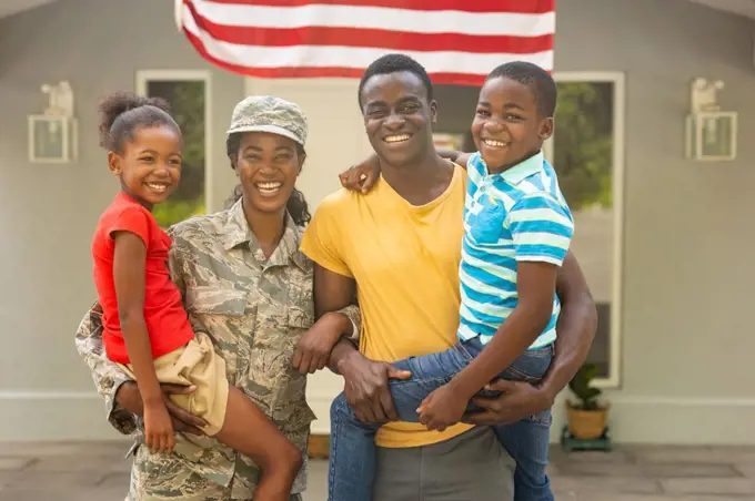 Portrait of happy female mid adult african american soldier with family outside house. unaltered, pride, homecoming, military, arrival, togetherness, armed forces and patriotism concept.