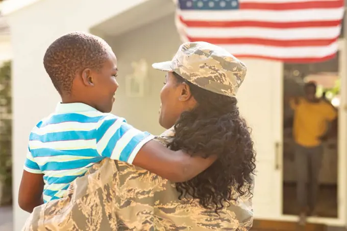 Happy female mid adult african american soldier carrying son on arrival at home. unaltered, pride, military, arrival, homecoming, armed forces and patriotism concept.