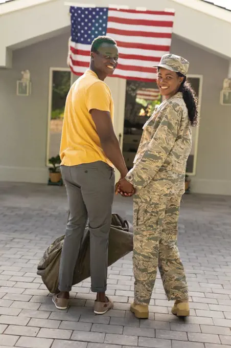 Portrait of smiling female mid adult african american soldier holding hand of husband on arrival. unaltered, pride, homecoming, american flag, military, arrival, armed forces and patriotism.
