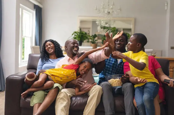 Happy african american multi-generational family high-fiving while watching rugby match on tv. unaltered, lifestyle, sport, fans, family, watching tv, rugby match, cheering and leisure concept.