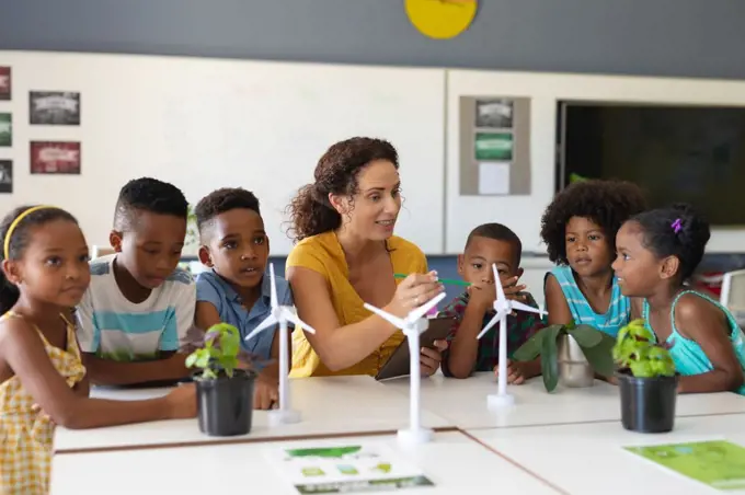 African american elementary students listening to caucasian young female teacher showing windmill. unaltered, education, environment, teaching, sustainable lifestyle and school concept.