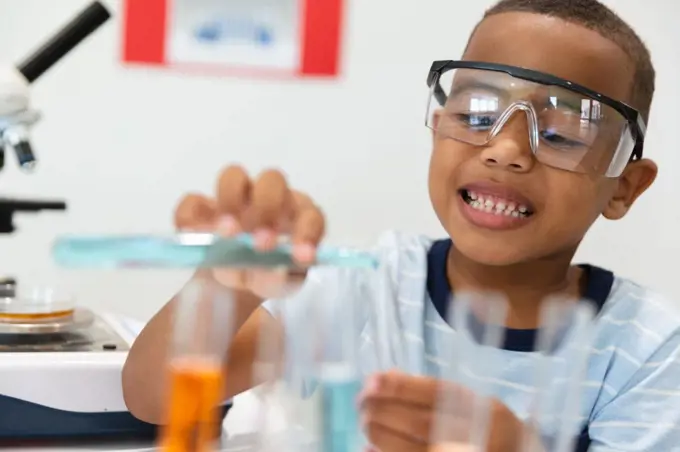 Smiling african american elementary schoolboy performing chemistry practical in laboratory. unaltered, education, laboratory, stem, scientific experiment, protection and school concept.