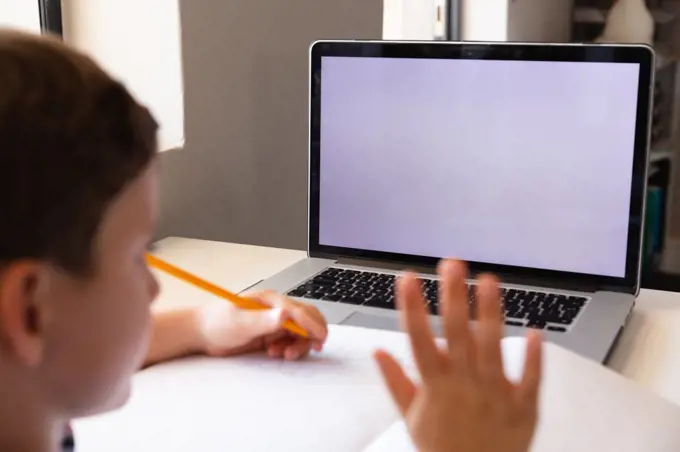 Caucasian elementary schoolboy waving hand on laptop while studying over video conference. unaltered, copy space, education, connection, childhood, studying, wireless technology and school concept.