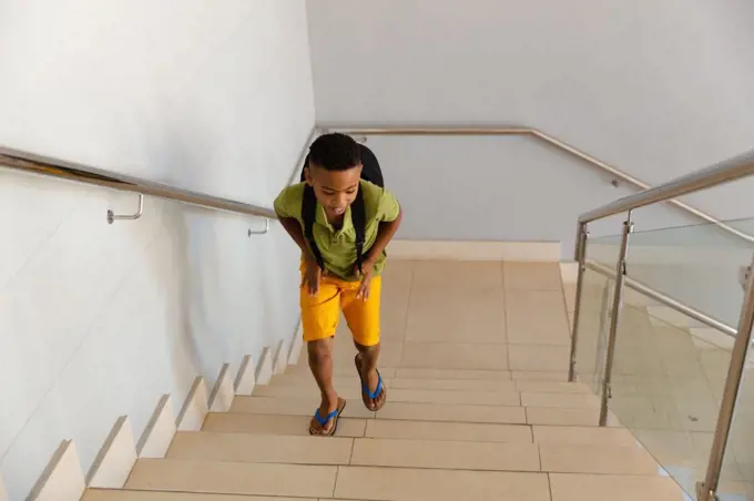 High angle view of african american elementary schoolboy with backpack climbing steps in school. unaltered, education, childhood and school concept.