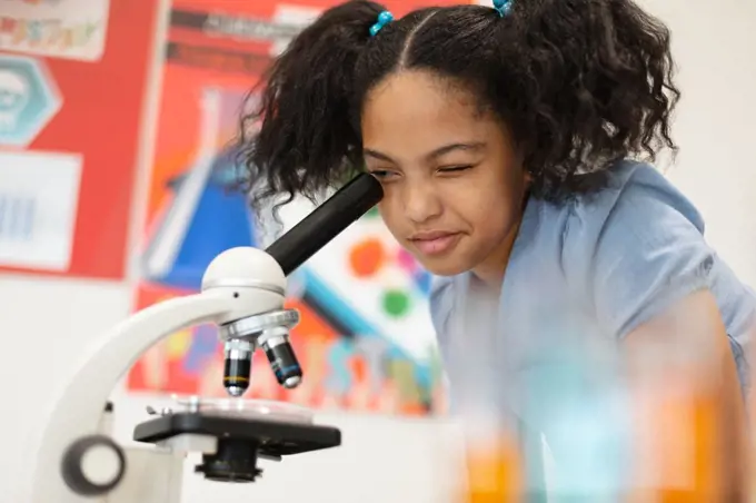 Biracial elementary schoolgirl looking through microscope during science practical class. unaltered, education, learning, scientific experiment, stem and school concept.