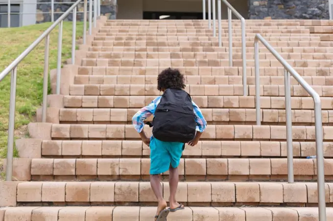 Rear view of african american elementary schoolboy with backpack climbing school building steps. unaltered, childhood, education and school concept.