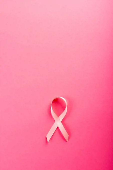 Overhead view of pink breast cancer awareness ribbon isolated against pink background. copy space. pink, breast, cancer, medical, ribbon, awareness, support, healthcare and alertness concept.