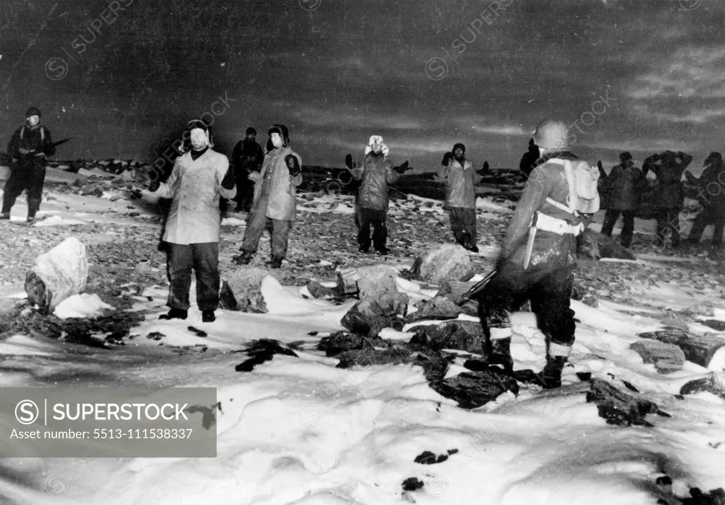 Germans Captured on Greenland: Coast guardsmen guard a group of German prisoners who raise their hands in surrender following their capture during recent action on Greenland. The Germans were attempting to establish and maintain radio-weather stations in the area. The coast guardsmen accounted for the capture of 60 German prisoners, destruction of two enemy bases, capture of a new armed trawler and the scuttling of another with a third abandoned in the ice. December 14, 1944. (Photo by Associate
