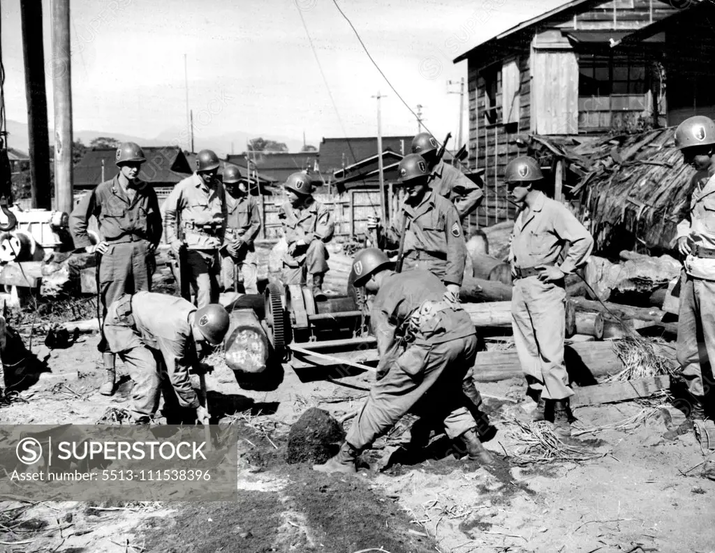 GIs Find Silver Cache in Jap Junk Yard: Yanks of the 132nd Infantry "American" division stand by as two of their buddies uncover a hidden trap door leading to a silver cache in a Japanese junk yard. Discovery of the cache followed a tip as to its whereabouts under a few feet of dirt and discarded machinery. December 3, 1945. (Photo by Associated Press Photo).