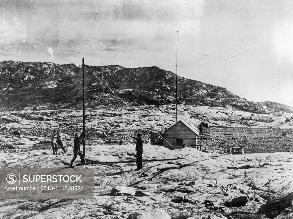 British Arctic Air Route Expedition: A view of the hut built at the Base Camp of the Expedition at Sermilik Fjord, about 80 miles from Angmagsalik. Capt. P. Lemon the wireless operator is seen directing the erection of the second wireless mast. October 25, 1930. (Photo by British Arctic Air Route Expedition Photograph).