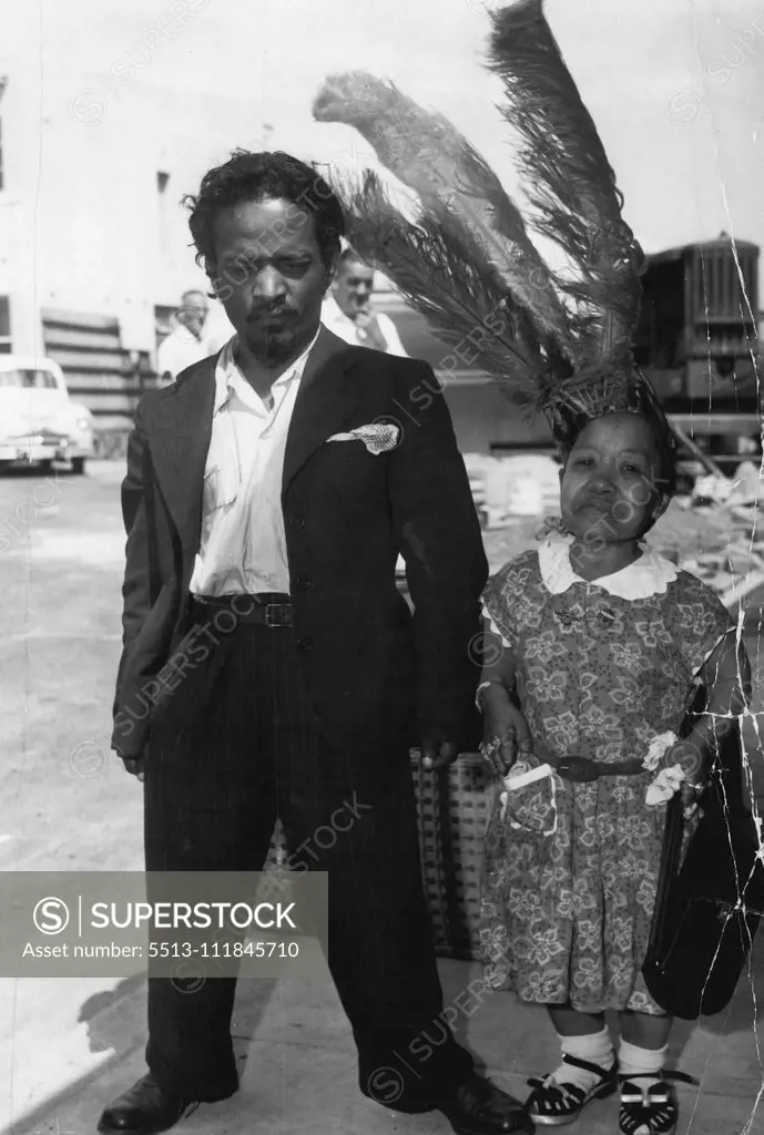 Arabi Ben Akba, 32, Ubangi Chilliwingi African midgets arrive by air in Sydney for the R.H.S. Show. African pigmy Arabi Ben Akba (pictured with Ubangi), had to talk fast at home to join ***** travelling side *****. February 21, 1955.;Arabi Ben Akba, 32, Ubangi Chilliwingi African midgets arrive by air in Sydney for the R.H.S. Show. African pigmy Arabi Ben Akba (pictured with Ubangi), had to talk fast at home to join ***** travelling side *****.