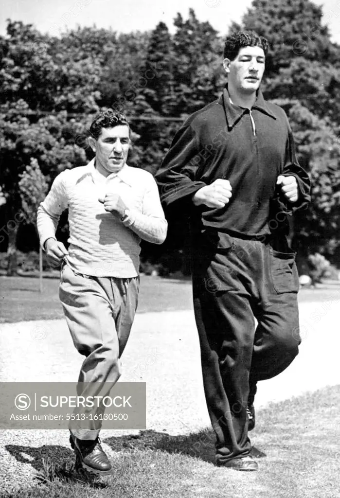 South African boxer Ewart Potgieter towers over his trainer John Holt in an exercise run at Brighton, England. Potgieter is 7ft 2in high and weighs 22½st. August 27, 1955.