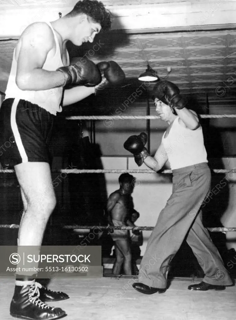 Potgieter tower over his trainer, former South African bantam champion Johnny Hold at they shape up in the gymnasium. February 18, 1955.