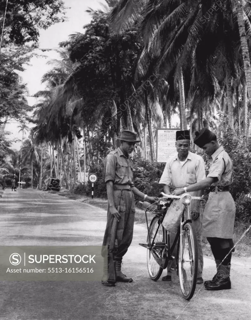 Because of the Emergency it is forbidden to take food out of the New Villages and the penalties for being caught are very severe. Control points are established on the exits and entrances of the new villages and on main roads. Here a Malay Home guard with rifle and a Malay policeman are shown checking a Malay civilian passing through a New Village area. December 19, 1955. (Photo by Ross/Fairfax Media).