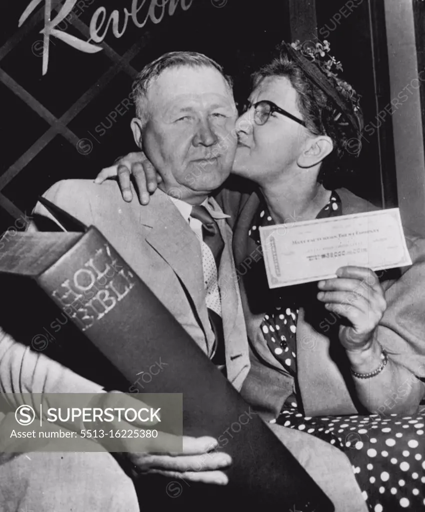 For $32,000 She Does The Kissing - While her husband, James, holds huge Bible, Mrs. Catherine Kreitzer, 54-year-old Camp Hill, Pa., grandmother, bestows kiss on his check after electing to take $32, 000 instead of going on for $64,000 on television quiz show here tonight. Mrs. Kreitzer, who chose the Bible for her subject, used biblical quotation on moderation as basis for turning back from the big prize. July 12, 1955. (Photo by AP Wirephoto).