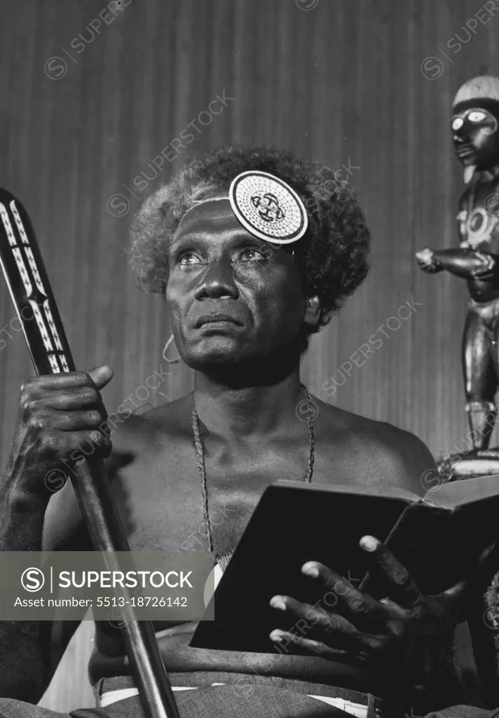 Before a heathen idol, Ragose poses, Bible in one hand, head-hunter's club in the other. The erenge (piece of island money) which is strapped on his forehead was worth 20 sovereigns in his father's day.Head hunter's club in one hand, a bible in another. Behind him stands a typical solomons Island idol, a blades evil eyed demon which the heather nation used to worship. Tied to his forehead is an ERENGE, a piece of island money worth 20 golden sovereigns in his father's day. June 02, 1954.