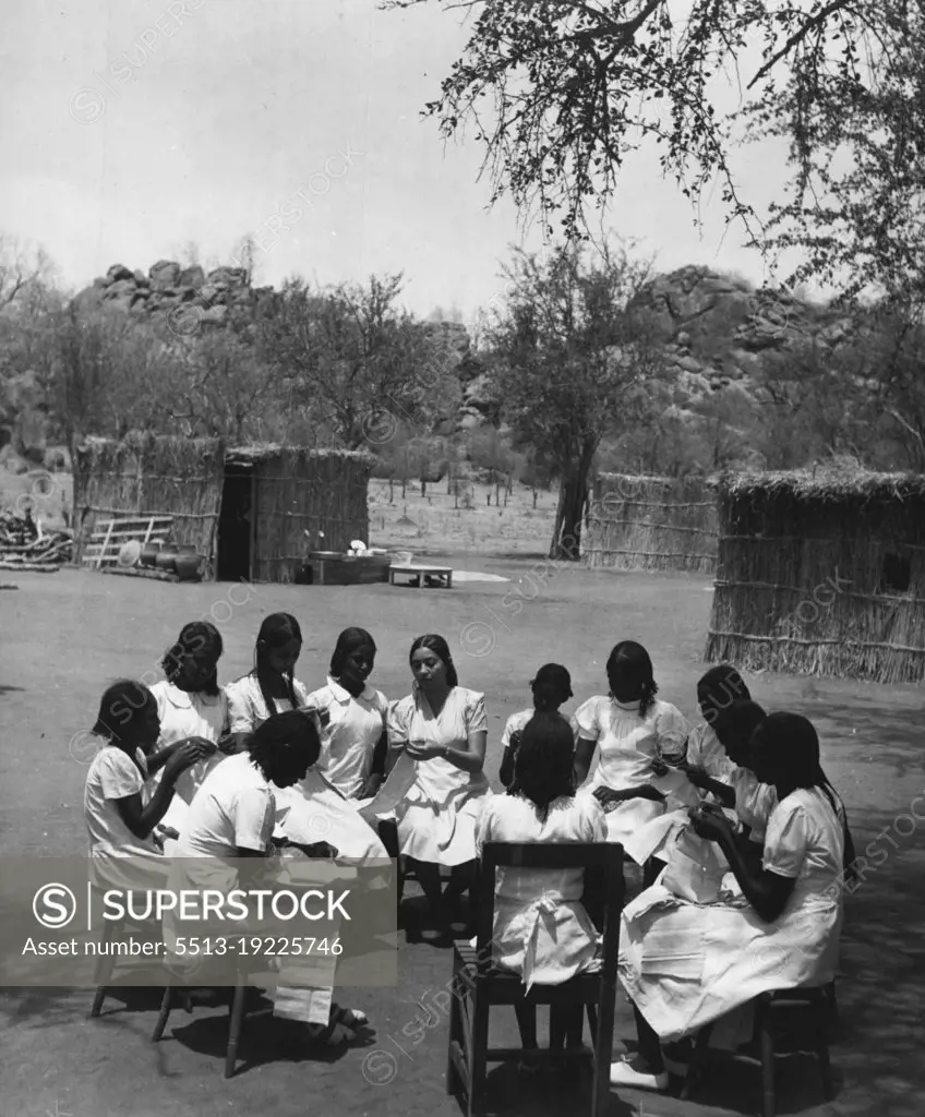 Sudanese Girls Train To Be Teachers.They Learn In Grass Hut Classrooms Until New College Is Ready.The sewing class sits in a circle round the teacher outside the grass huts which have been put up as temporary classrooms. These huts or tukls, are erected by Sudanese in a few hours. May 14, 1953. (Photo by Central Office Of Information).