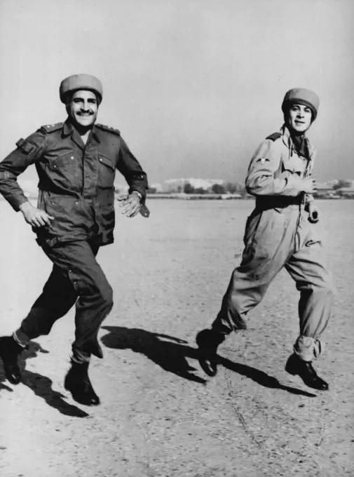 Egyptian Paratroopers Stage First Mandeuvers Captain Steimel (right, first name not available), German Instructor, runs to the waiting aircraft with an Egyptian paratrooper, during the first manoeuvres of the newly created Egyptian paratroop unit, November 29th. A Dakota aircraft of the Egyptian Royal Air Force took off from the Almaza Military Airport, with four Egyptian parachutists during the manoeuvres and later the parachutists baled out over a field. German experts who for several months h