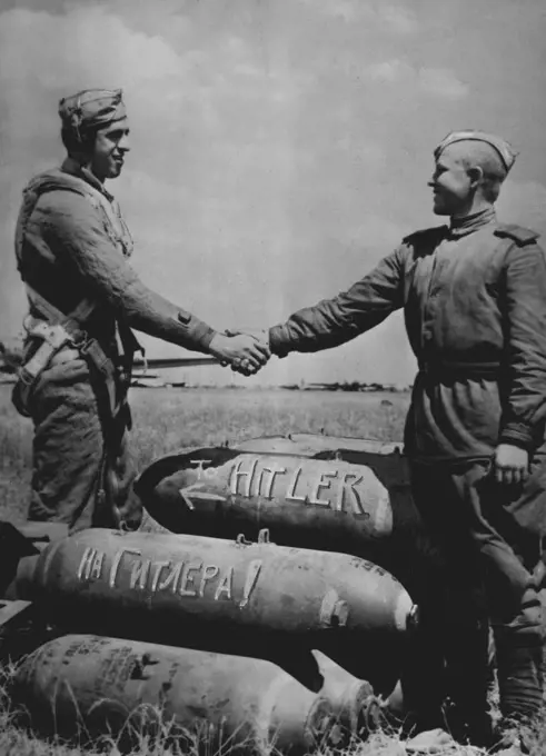 American And Russian Soldiers Shake Hands Over Bombs For The Enemy -- At an air base in Russia used by American aircraft, a U.S. and Red Army soldier shake hands over a pile of bombs addressed to the enemy. The Russian words "to Hitler" are painted on a bomb under one bearing the English spelling American aircraft have used bases in Russia since June 2, 1944, when Flying Fortresses left a base in Italy, bombed German targets in Rumania, and combined to new airfields in Russia prepared to receive