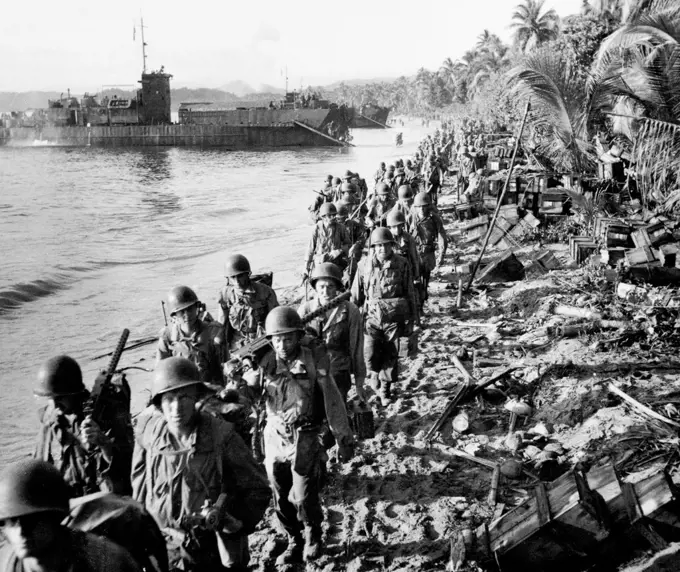 Along a beach littered with the remains of blasted Japanese dumps file American soldiers who successful attacked Japanese held Hollandia in Dutch New Guinea. April 25, 1944.