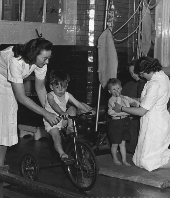 At Work - Judy Bulfin (left) puts 3½-year-old William Smith through a series of quadriceps exercise against his complaint, genu valgum (Knock-Knees). Judy is physiotherapist at world-famous Gt. Ormond Street for Sick Children, where the Department for Physical Medicine is doing important pioneer work. March 17, 1949. 
