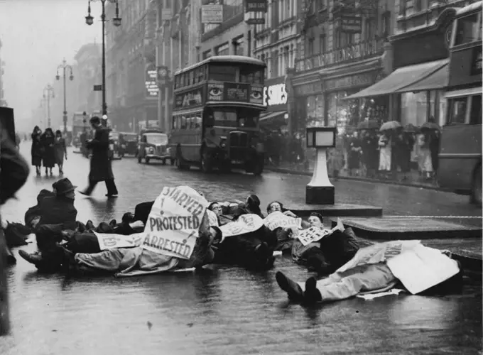 Unemployed Men Lie Down In Oxford Street -- The unemployed men lying in the road at the corner of Oxford Street and Berwick Street. Members of the Unemployed Workers Movement staged another demonstration today when they laid down in the road at the corner of Oxford Street and Berwick Street, holding up the traffic until the police dispersed them. January 17, 1939. (Photo by Keystone). 
